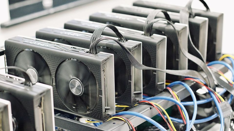 Rows of graphics cards mounted in an open-frame mining rig, linked by blue cables
