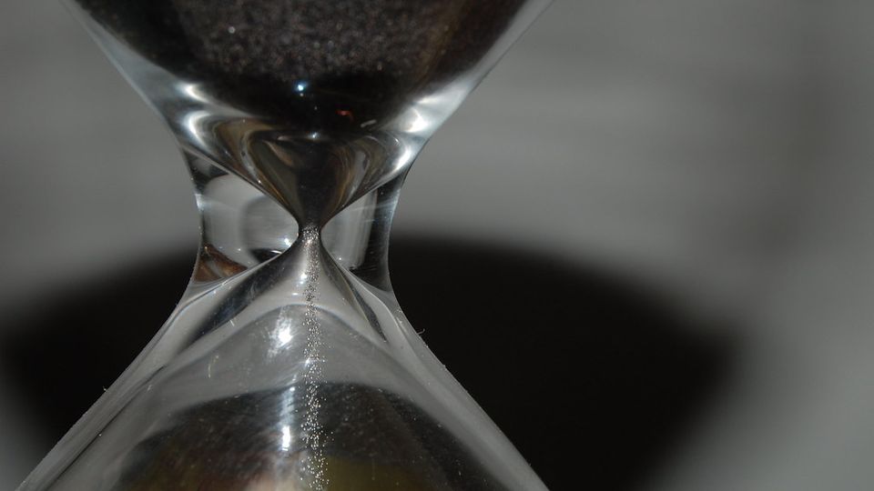 Close-up of an hourglass with dark sand running through the narrow neck