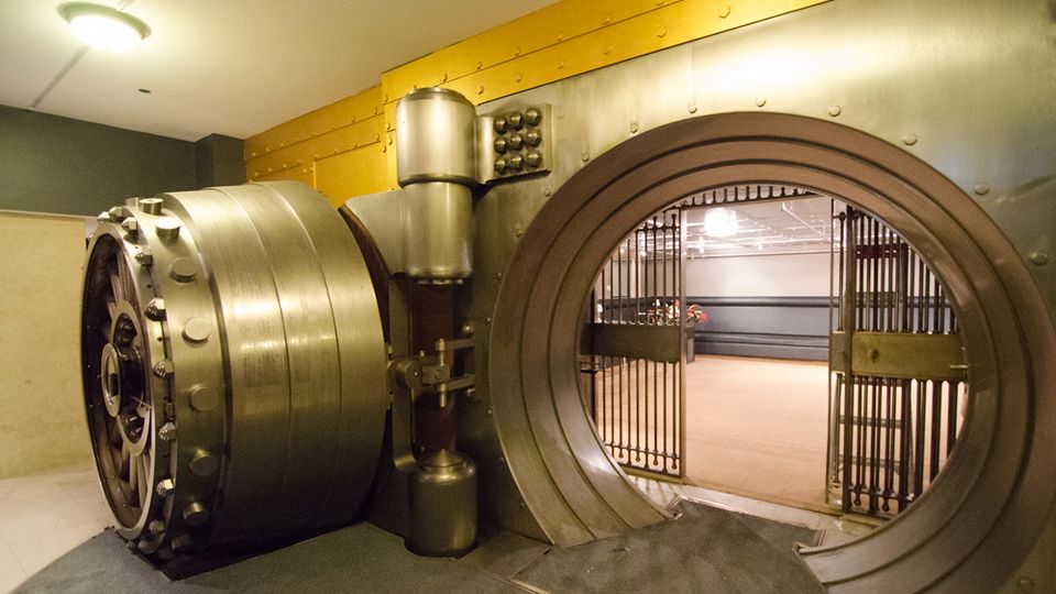 Open round steel vault door leading into a bank vault