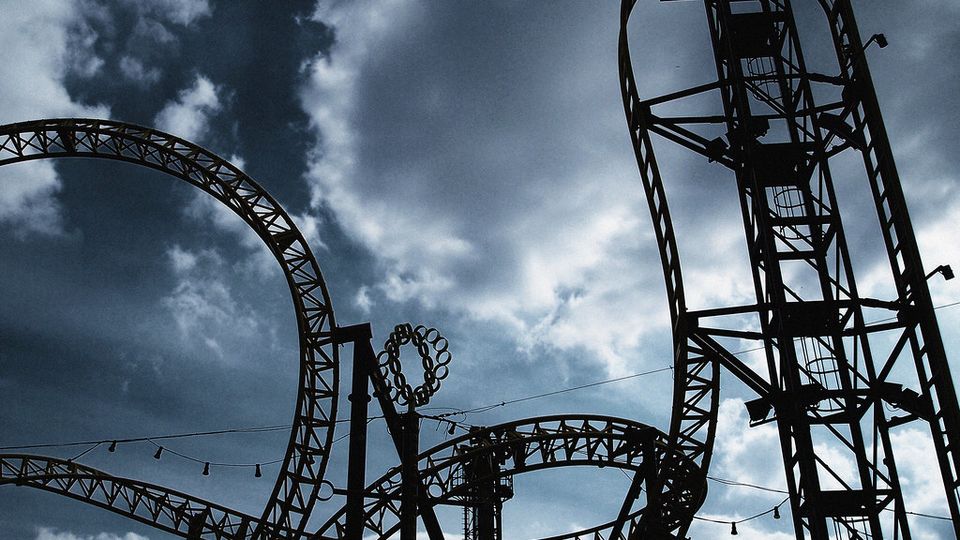 Silhouette of a roller coaster's loops against a cloudy sky