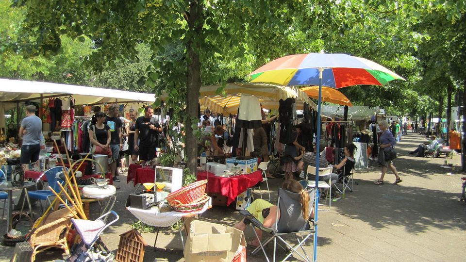 Open-air flea market with stalls under shady trees