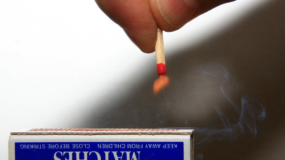 Hand striking a match above a matchbox