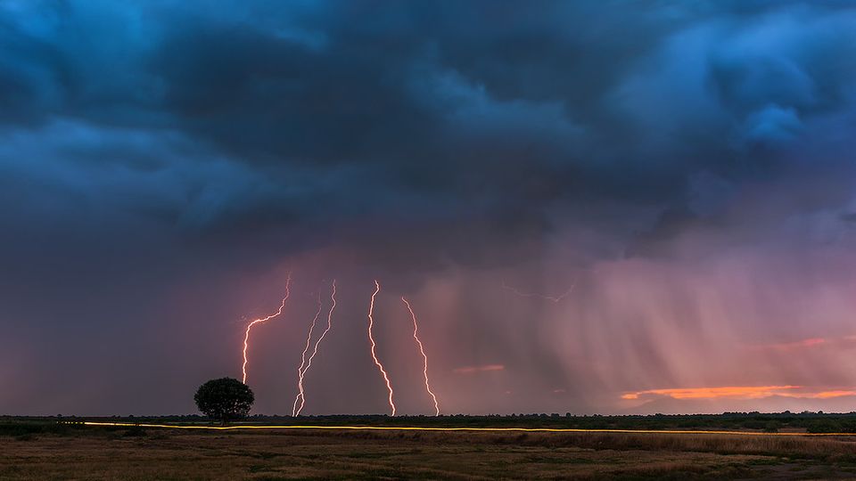 Several lightning bolts striking a flat landscape under storm clouds