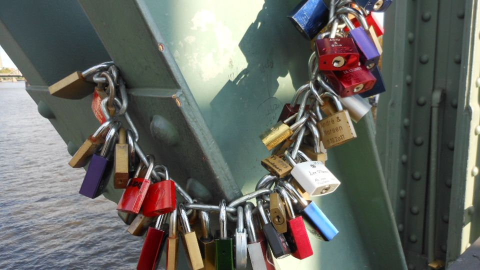 Padlocks of many colours locked onto a bridge railing above water