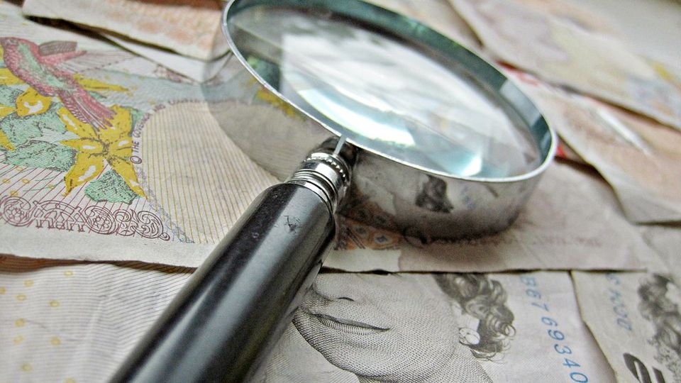 Magnifying glass held over banknotes and a map